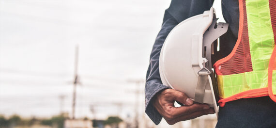 Trabalhador da construção civil com capacete de segurança e colete refletivo em ambiente de obra, representando cumprimento das normas de SSMA