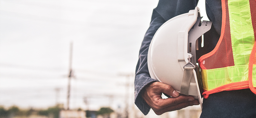 Trabalhador da construção civil com capacete de segurança e colete refletivo em ambiente de obra, representando cumprimento das normas de SSMA