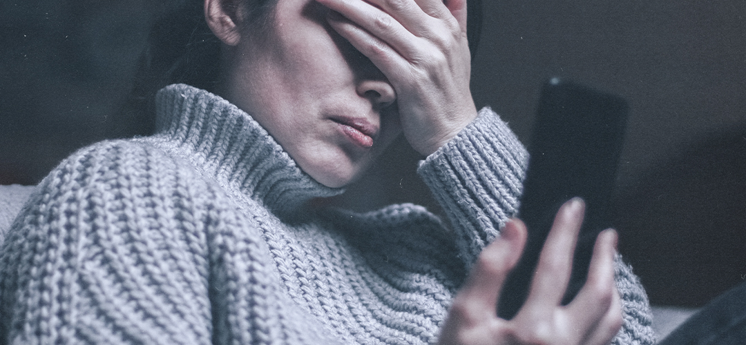 Pessoa olhando o celular com expressão de angústia, representando os impactos do uso excessivo das redes sociais na saúde mental.