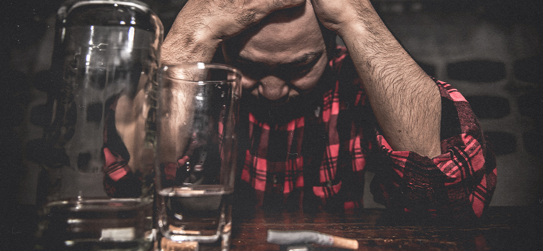 Homem com sinais de sofrimento emocional ao lado de copos de bebida alcoólica